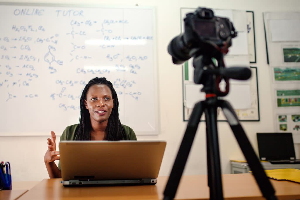 A woman uses a DSLR camera to record herself teaching during an online tutoring session. 