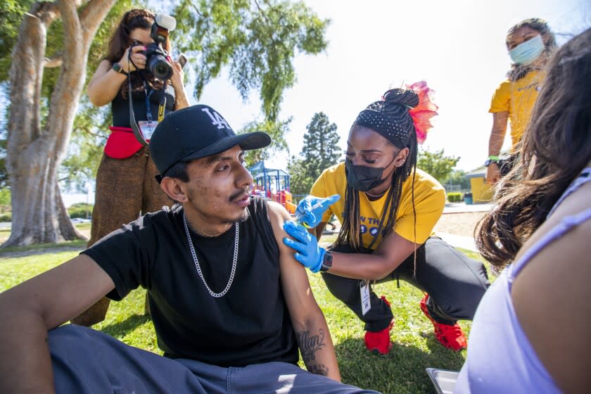 LOS ANGELES, CA - MAY 05: Asia Hartford, LVN, right, gives Luis Fernandez, 28, a vaccine in Ted Watkins Memorial Park on Thursday, May 5, 2022 in Los Angeles, CA. CDC Director Dr. Rochelle Walensky visted a health department vaccination site in the park. Afterwards she walked into the park and watches children and their parents being vaccinated in the park by an outreach team from the near by site. (Francine Orr / Los Angeles Times)