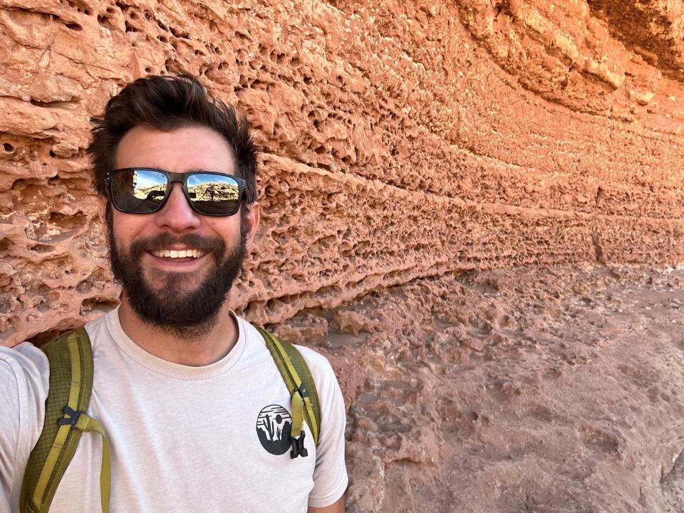 Keith Media wearing sunglasses and a backpack taking a selfie in front of a mountain.