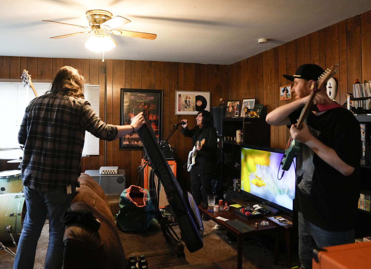 Santos Enrique Camara, center, smiles as he practices at his home with Jack Thompson, left, and Phil Westfall, right, with their band The Lion & The Sloth Thursday, March 23, 2023, in Marysville, Wash. Camara, 27, who dropped out of Shoreline Community College in 2015 after completing one semester studying audio engineering, had difficulty paying tuition and finding time to do schoolwork while caring for his younger sister. "I seriously tried," he said. "I gave it my all." For now, Camara is happy working as a sous-chef and cook at a local restaurant while planning a tour with one of his two bands. (AP Photo/Lindsey Wasson)