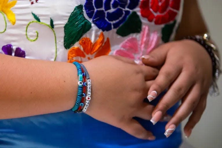 Karina Garcia wears a bracelet that bears her father’s nickname as she tries on her quinceañera dress on Nov. 20 in Juárez. Her friend and teammate Genesis, who was also coached by Memo, made the bracelet for her.