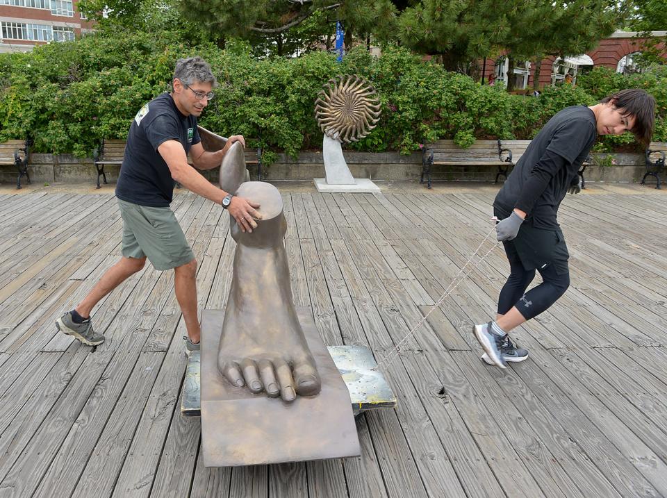 Sculptor Michael Alfano, left, of Hopkinton, and his assistant, Yerzat Tleulin, transport Winged Foot, one of 20 sculptures in the "Of Many Minds" waterfront sculpture walk at the Charlestown Navy Yard, on June 16. The exhibit runs through December 2023. In the background is a sculpture titled Running Wheel.