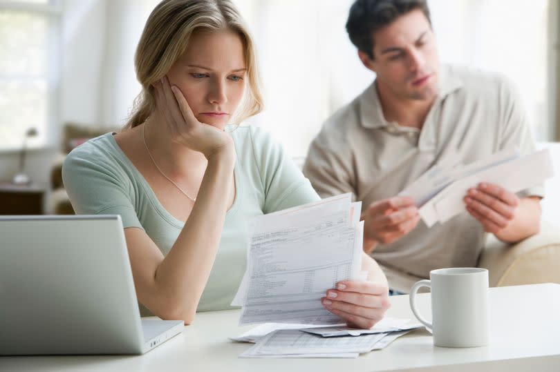 A young couple looking at bills and paperwork, next to a laptop and coffee mug