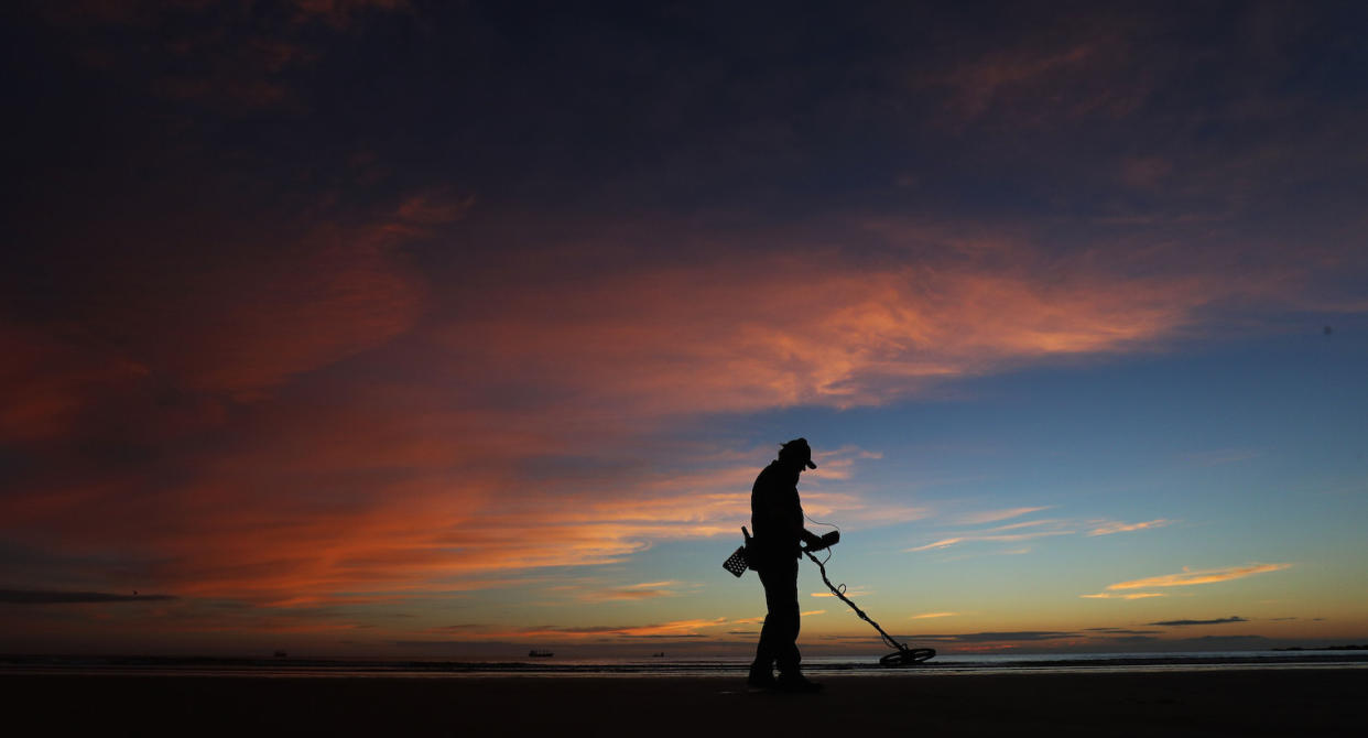 A man with a metal detector on Tynemouth Beach, Tyne and Wear, as dawn breaks.