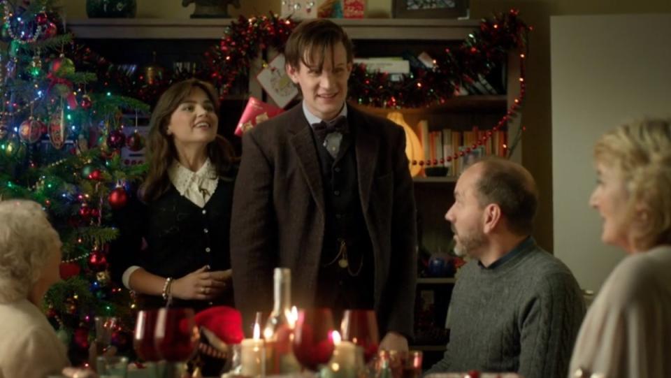 clara and the eleventh doctor stand in front of a christmas tree and fireplace with her parents sitting at a table in front of them