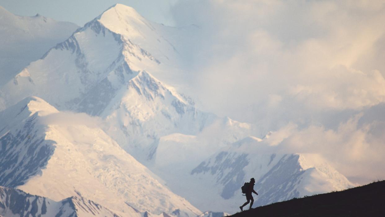  A man hikes in front of a snow-covered mountain in Denali National Park and Preserve in Alaska. 