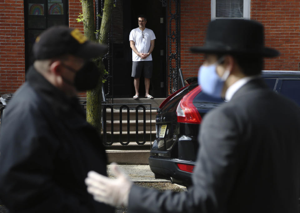 FILE - In this May 3, 2020, file photo, Paul Catanzaro stands in his doorway across the street from Scotto Funeral Home, praying alongside a small group gathered to say goodbye as the body of the Rev. Jorge Ortiz-Garay is prepared for transport in the Brooklyn borough of New York. Ortiz-Garay was the first Catholic cleric in the United States to die from the coronavirus outbreak. He was recently flown to Mexico City where his body was laid to rest. (AP Photo/Jessie Wardarski, File)