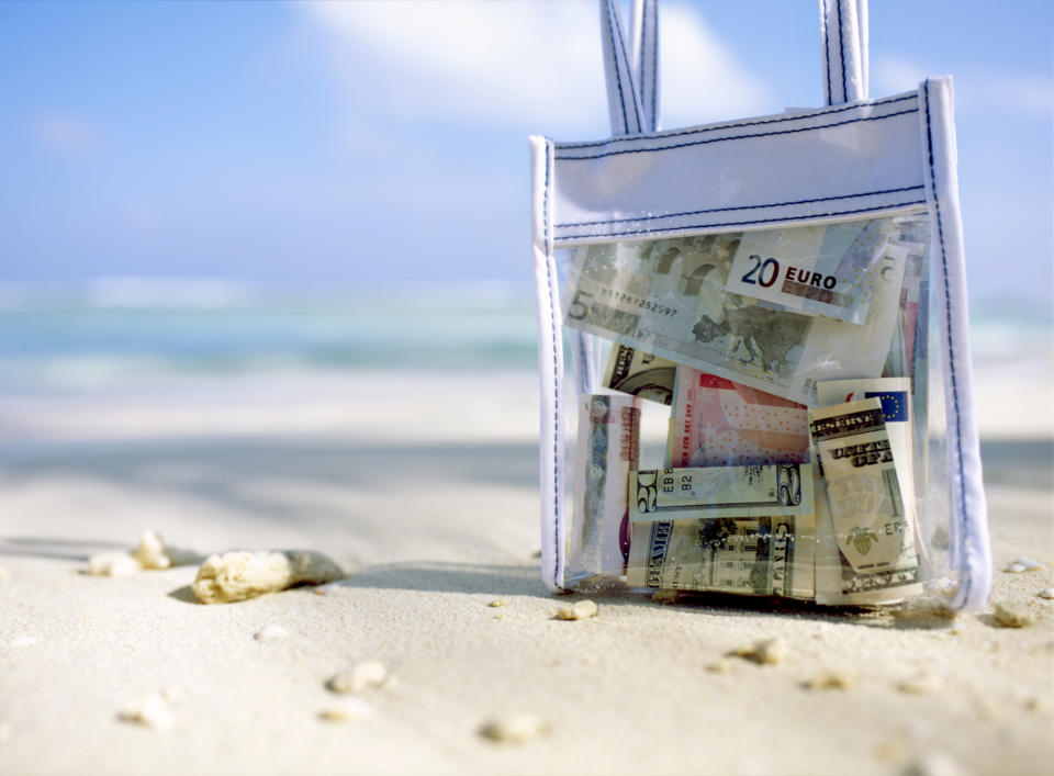 Transparent bag with money and postcards on a sandy beach, travel concept