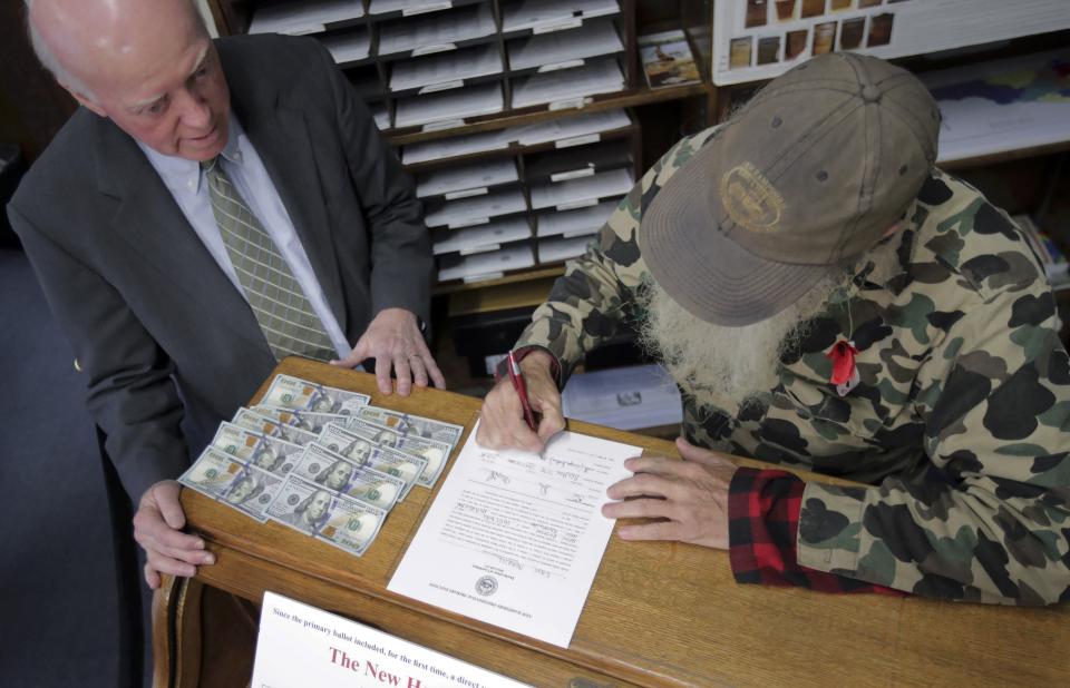 FILE - In this Friday, Nov. 8, 2019, file photo, Republican Eric Merrill, right, of New Boston, N.H., paid the filing fee of $1,000 in cash as he files to have his name listed on the New Hampshire presidential primary ballot in Concord, N.H. At left is New Hampshire Secretary of State Bill Gardner. The quadrennial chaos has quieted down at the New Hampshire secretary of state’s office with the closing of the filing period for the first-in-the-nation presidential primary. (AP Photo/Charles Krupa, File)