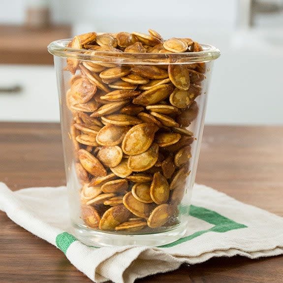 Roasted pumpkin seeds in a glass cup sitting on a wooden table.