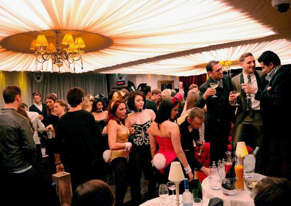 In this undated photo provided by Playboy.com, Playboy Bunnies and guests mingle in London's club, which opened in 2011 following a 30 year hiatus. The tightly corseted Playboy Bunnies, with rabbit tails and ears, will soon be back in business in New York City. Three decades after the original Playboy Club closed in Manhattan, a new club will debut later 2017 in a hotel a few blocks from Times Square. (Playboy.com via AP)