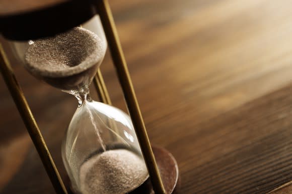 Sand filtering from the top to the bottom of an hourglass that's sitting on a wooden table.