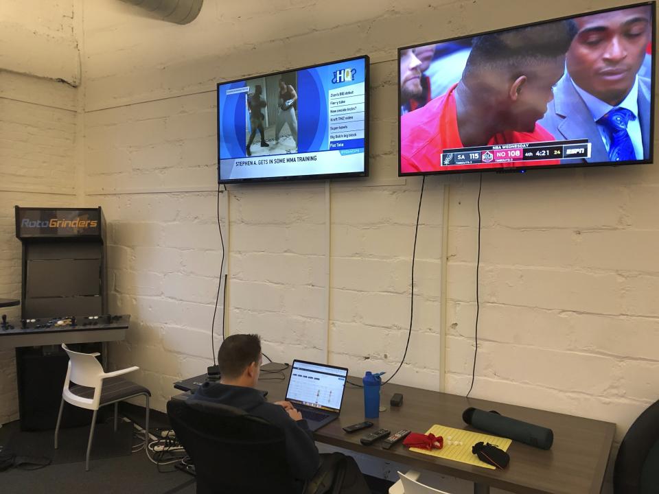 In this undated image provided by Cameron MacMillan, Brian Hourigan works at the Better Collective Tennessee, RotoGrinders.com office in downtown Nashville, Tenn., as NCAA college basketball plays on a television screen above. Sports can be a distraction at work the first few months of the year as pro football and college basketball hold their premier events. Business owners have to make a choice, whether, like McMillan at RotoGrinders.com, they'll allow or encourage staffers to enjoy the moment, or demand that everyone focus on work. (Cameron MacMillan via AP)