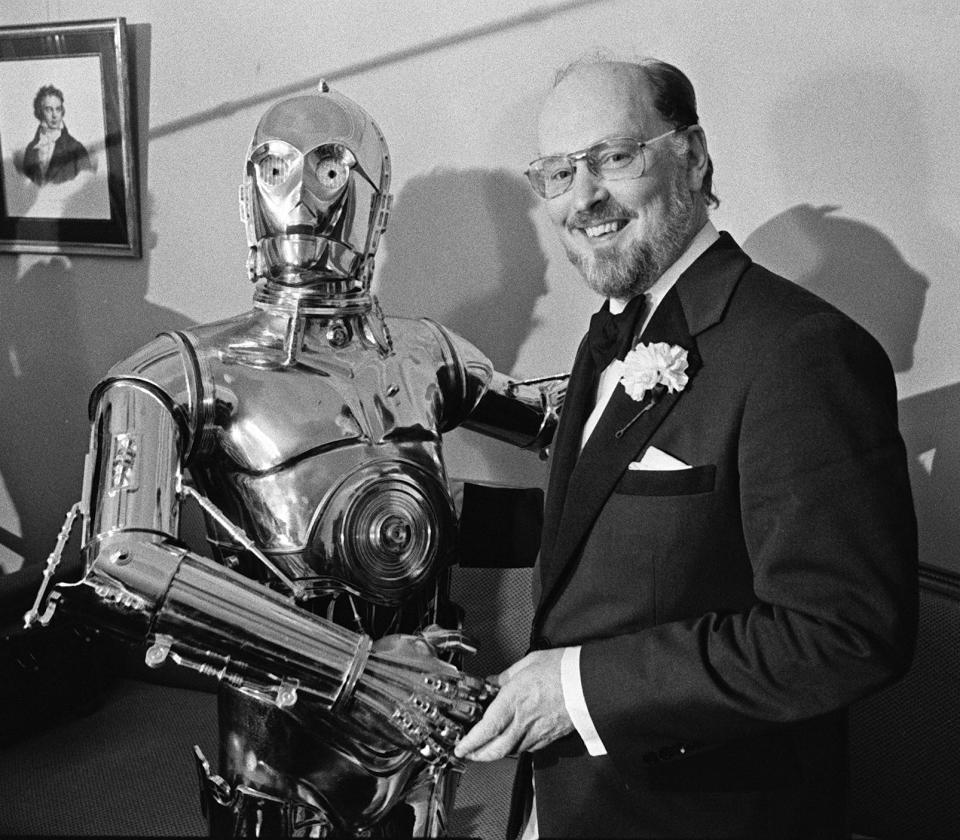 FILE - Boston Pops conductor John Williams, right, shakes hands with "Star Wars" character C-3PO at a news conference in Boston on April 30, 1980. Williams, 90, is devoting himself to composing concert music, including a piano concerto he’s writing for Emanuel X. This spring, he and cellist Yo-Yo Ma released the album “A Gathering of Friends,” recorded with the New York Philharmonic.(AP Photo, File)