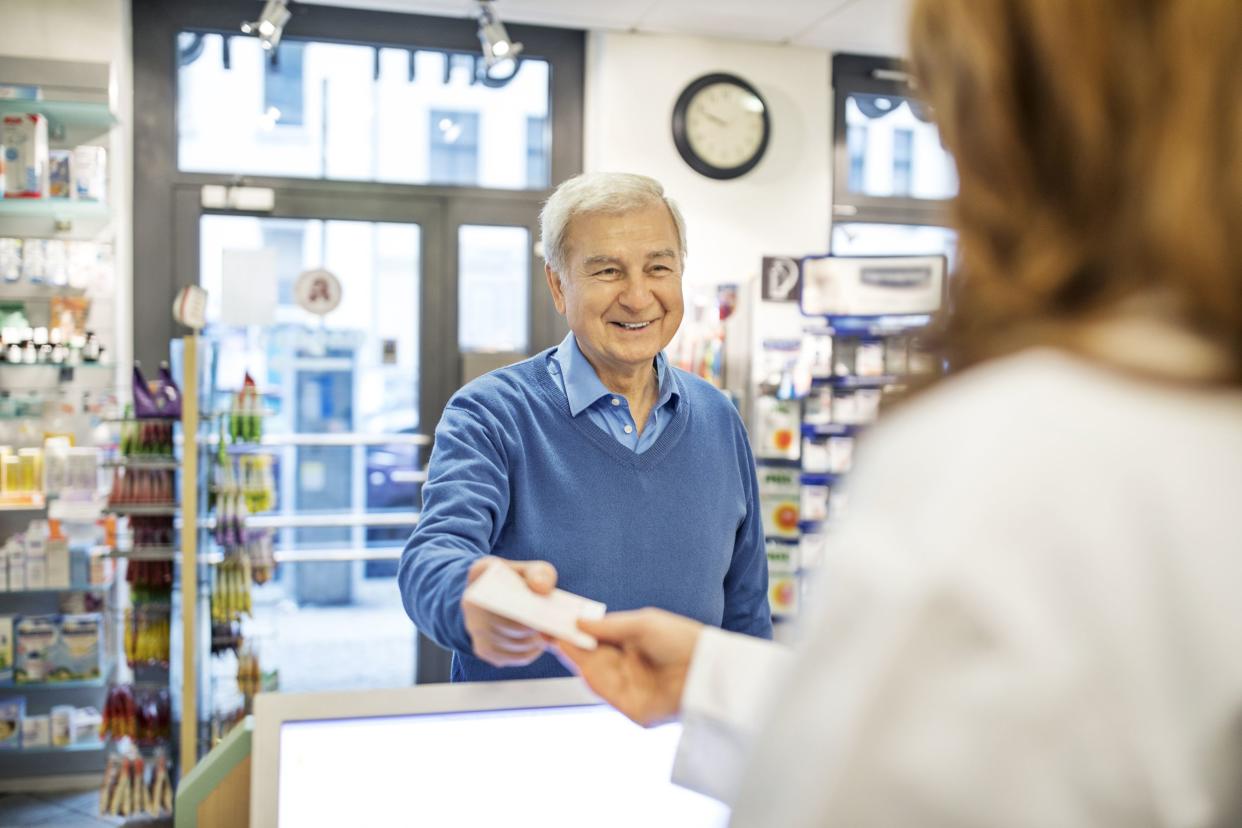 smiling senior man giving prescription to pharmacist