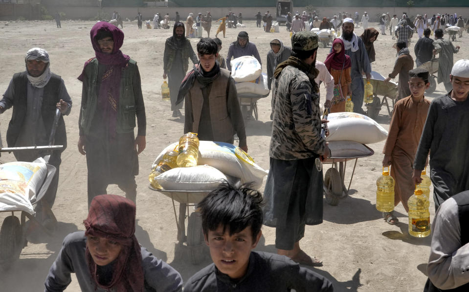 FILE - A Taliban fighter stands guard as people receive food rations distributed by a Chinese humanitarian aid group, in Kabul, Afghanistan, Saturday, April 30, 2022. Two U.N. food agencies issued stark warnings on Monday, June 6, 2022 about multiple, looming food crises on the planet, driven by climate “shocks” like drought and worsened by the repercussions of the COVID-19 pandemic and the war in Ukraine that have sent fuel and food prices soaring. (AP Photo/Ebrahim Noroozi, File)