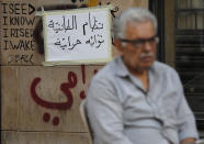 In this Thursday, Nov. 7, 2019, an anti-government protester sits in front of an Arabic placard that reads, "Sectarian system its lawmakers are thieves," in downtown Beirut, Lebanon. Lebanon’s protests have brought out people from across the country’s spectrum of faiths and communities trying to throw out the entire ruling elite. They give a glimpse into a Lebanon transcending longtime divisions among Muslims, Christians and other sects. (AP Photo/Hussein Malla)