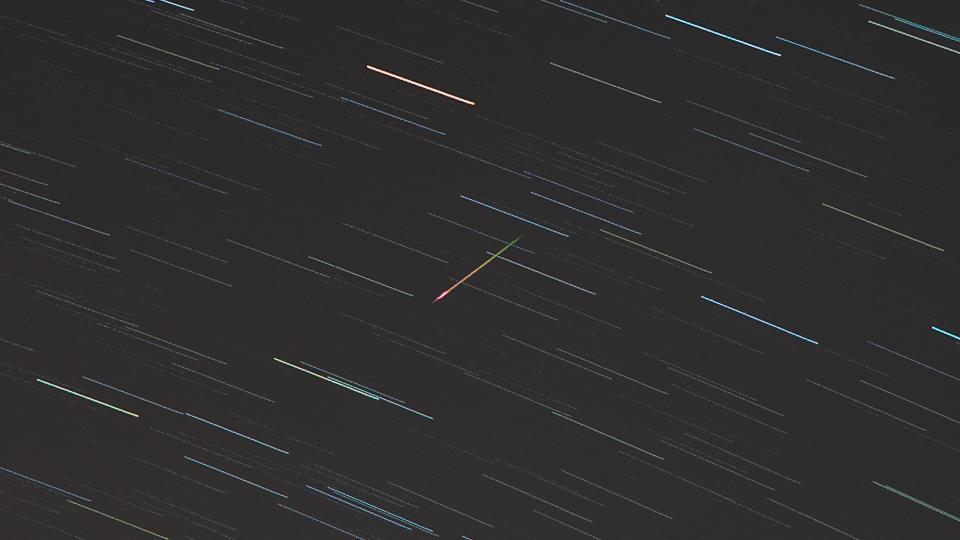 a streak of green light passes in front of background stars in the night sky