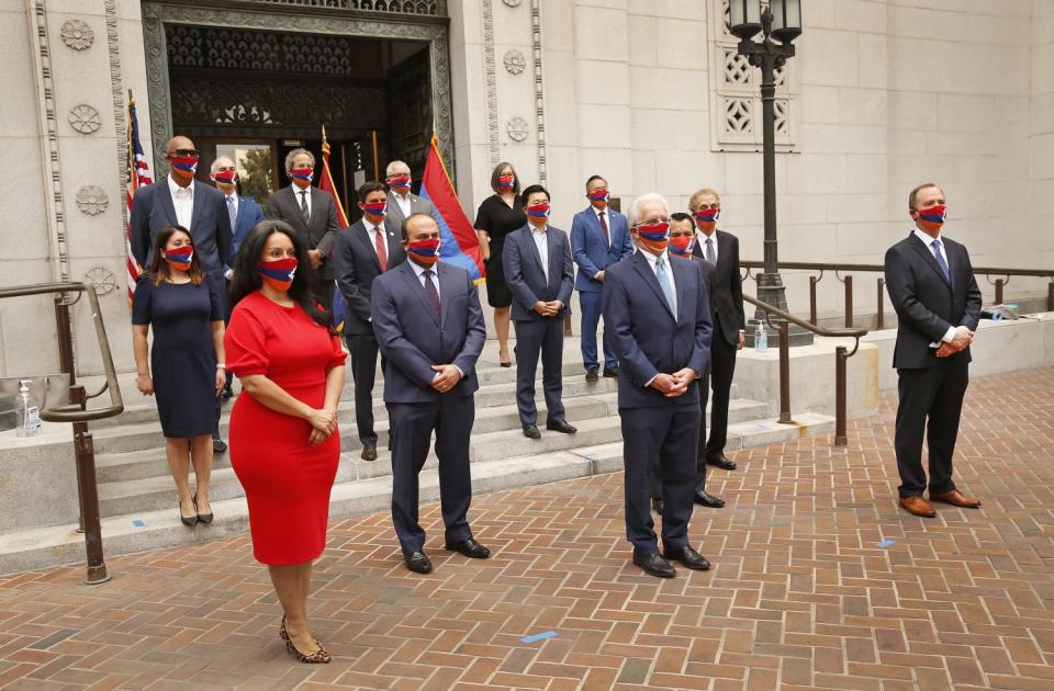 Local officials stand in masks and hold a flag outside L.A. City Hall