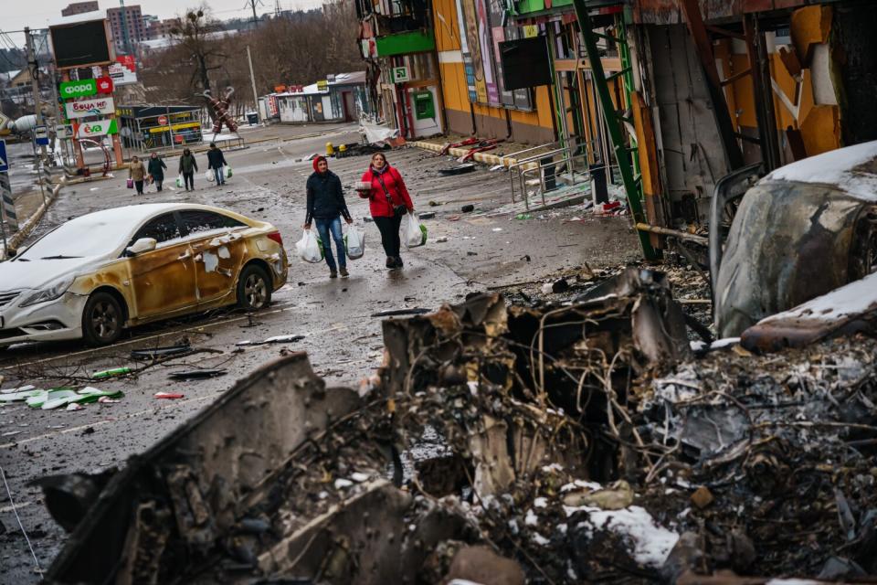 Residents carrying supplies walk back from the direction of Bucha, amid the debris of battle with Russian forces