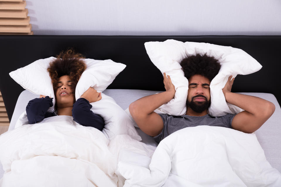 Young couple lying Inbed covering their ears with a pillow