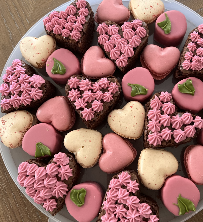 Heart-shaped decorated cookies and brownies with pink and green icing arranged on a round plate