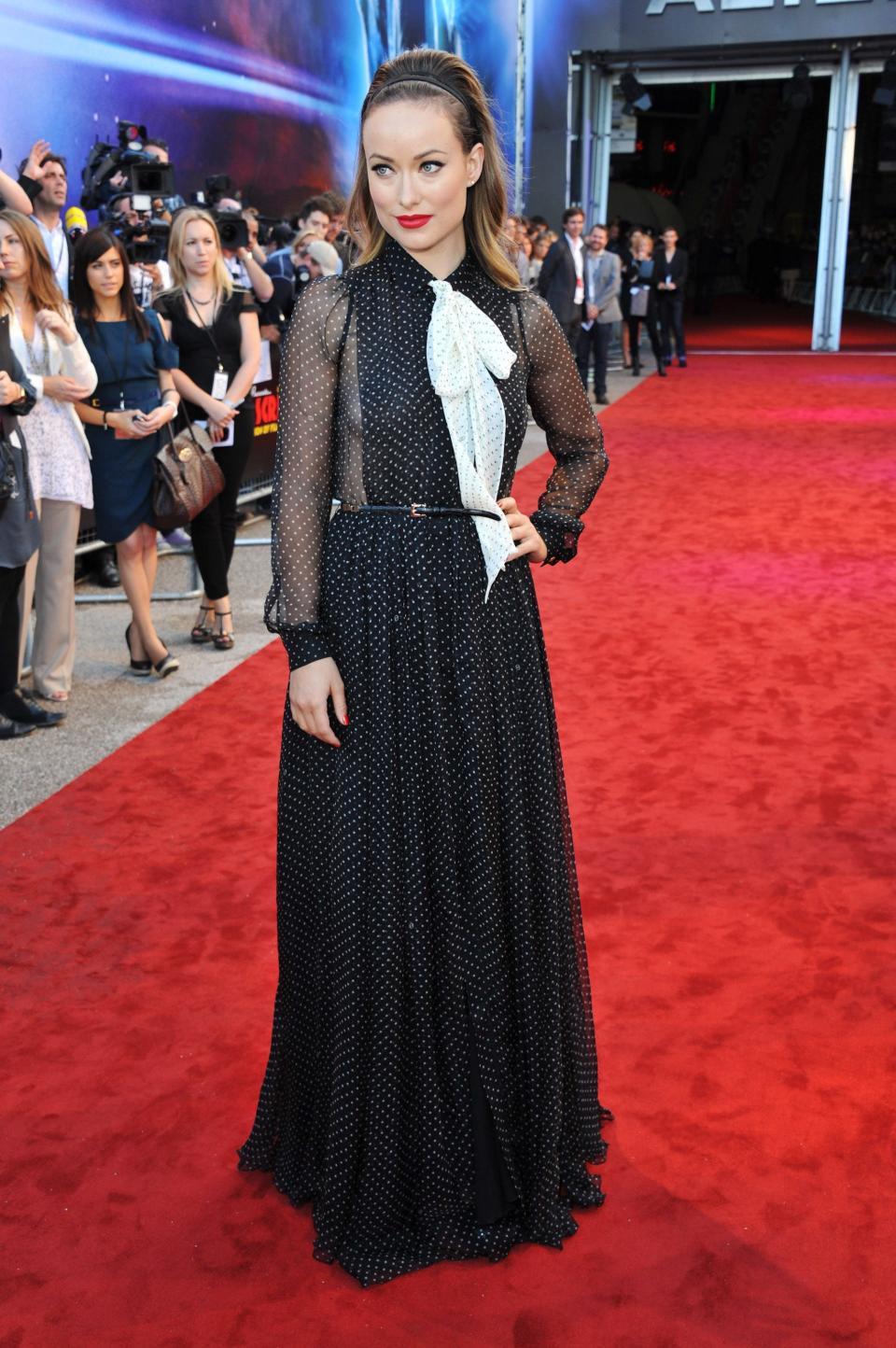 Olivia Wilde wears a black dress on a red carpet.