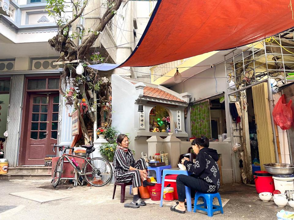 Two women sitting on blue chairs at noodle shop in Hanoi