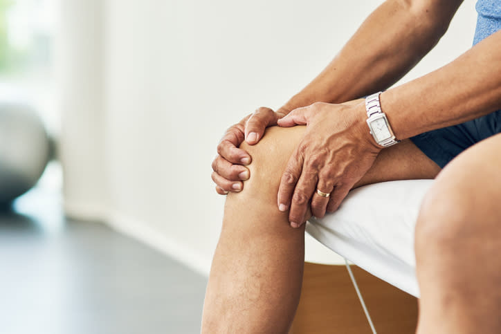 A person sitting and holding their knee with both hands, suggesting possible knee pain or discomfort