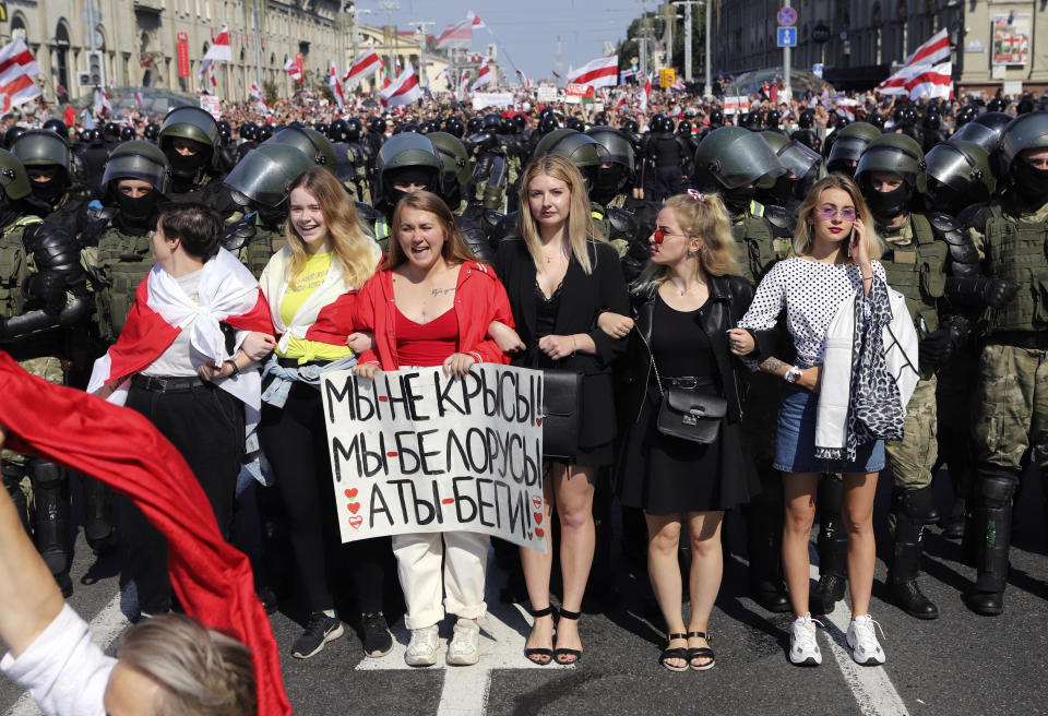 Women hold a poster reading "We are not rats, we are Belarusians, you (Lukashenko) run!" as they stand in front of riot police line blocking Belarusian opposition supporters rally in the center of Minsk, Belarus, Sunday, Aug. 30, 2020. Opposition supporters whose protests have convulsed the country for two weeks aim to hold a march in the capital of Belarus. (AP Photo)