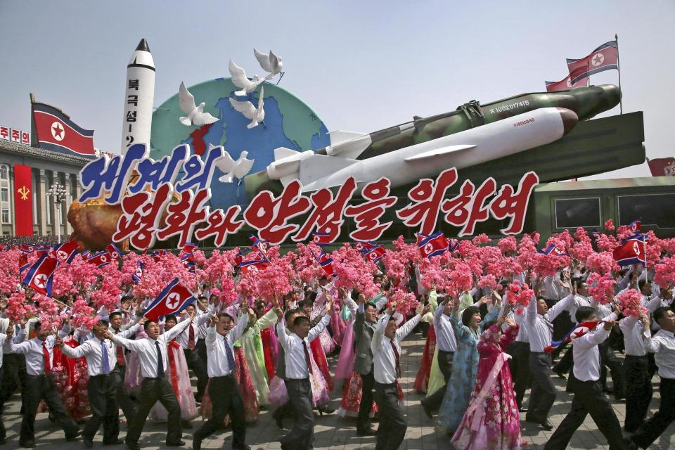 North Koreans wave flags and plastic flowers at a model missile parade: AP