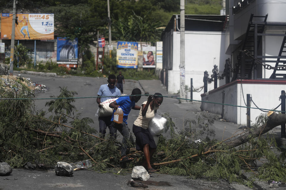 Residents walk through a barricade set up by protesters in Port-au-Prince, Haiti, Monday, Sept. 30, 2019. Opposition leaders are calling for a nationwide push Monday to block streets and paralyze Haiti's economy as they press for Moise to give up power, and tens of thousands of their young supporters were expected to heed the call. (AP Photo/Rebecca Blackwell)