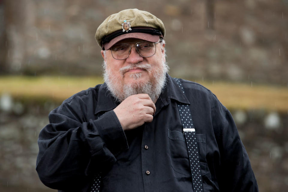 Man with beard in glasses and cap, hand on chin, thoughtful pose, wearing suspenders