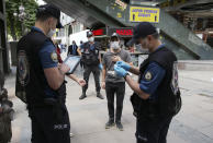 Police officers check a man's ID in the city center, in Ankara, Turkey, Thursday, June 18, 2020. Turkish authorities have made the wearing of masks mandatory in three major cities to curb the spread of COVID-19 following an uptick in confirmed cases since the reopening of many businesses.(AP Photo/Burhan Ozbilici)