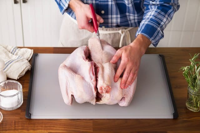 Person cutting the backbone out of a raw turkey carefully on a cutting board