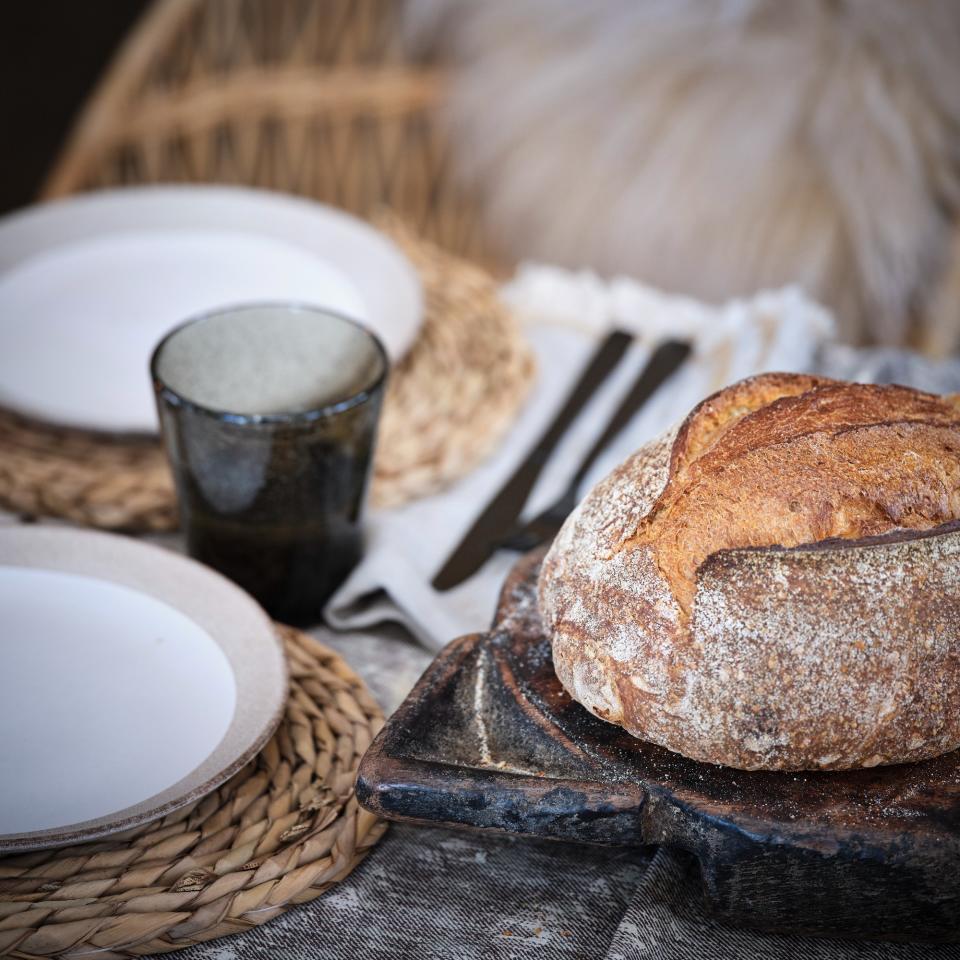 A dining table set with plates and cutlery and a loaf of bread