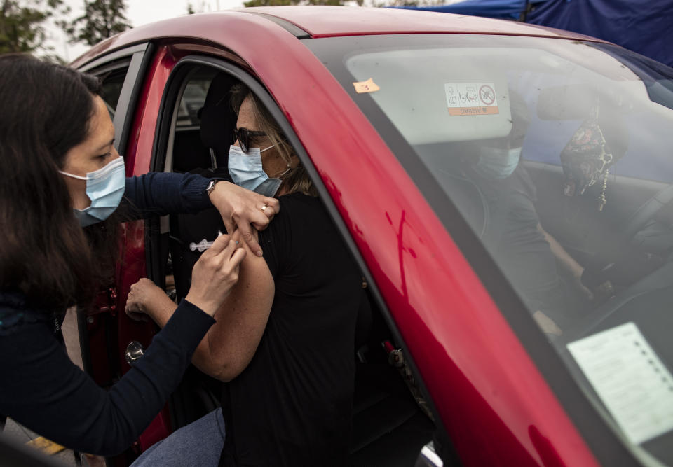 A healthcare worker injects a woman with a dose of the Sinovac COVID-19 vaccine at a drive-thru vaccination site at the National Stadium in Santiago, Chile, Tuesday, March 16, 2021. (AP Photo/Esteban Felix)
