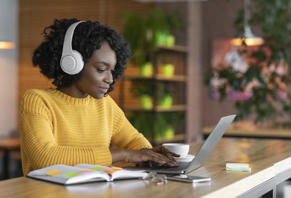 Young afro woman having online training, using laptop and wireless headset at cafe, free space