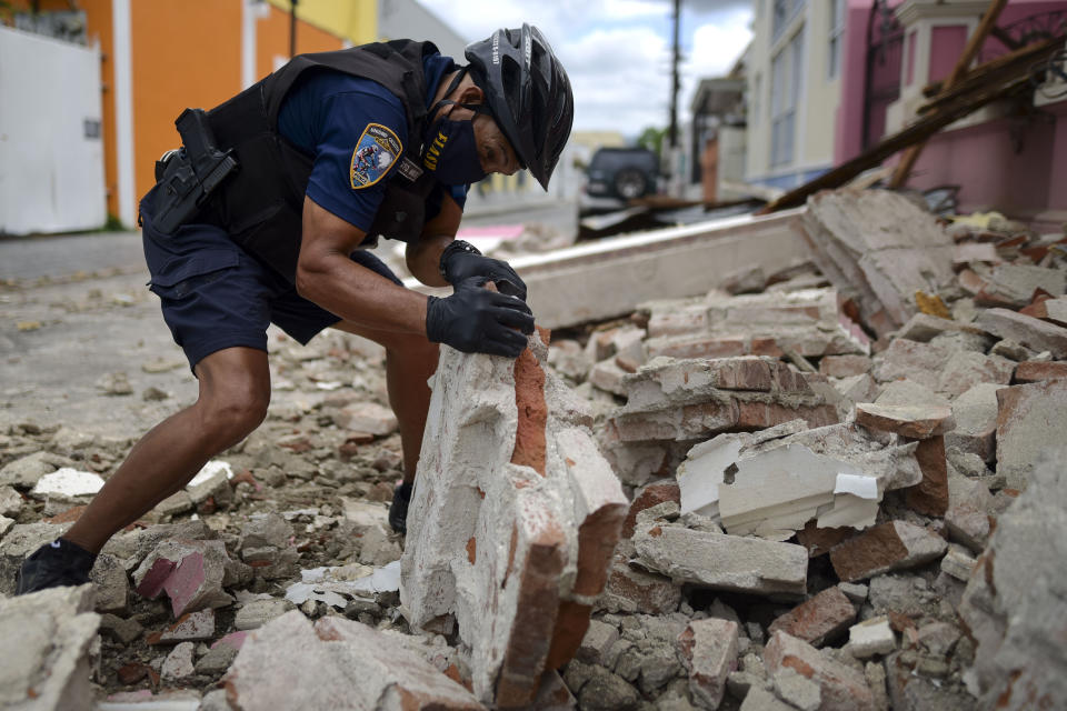 A police officer, wearing s protective face mask as a precaution against the spread of the new coronavirus, removes debris caused by a 5.4-magnitude earthquake, in Ponce, Puerto Rico, Saturday, May 2, 2020. The quake hit near southern Puerto Rico, jolting many from their beds on an island where some people still remain in shelters from previous quakes earlier this year. (AP Photo/Carlos Giusti)