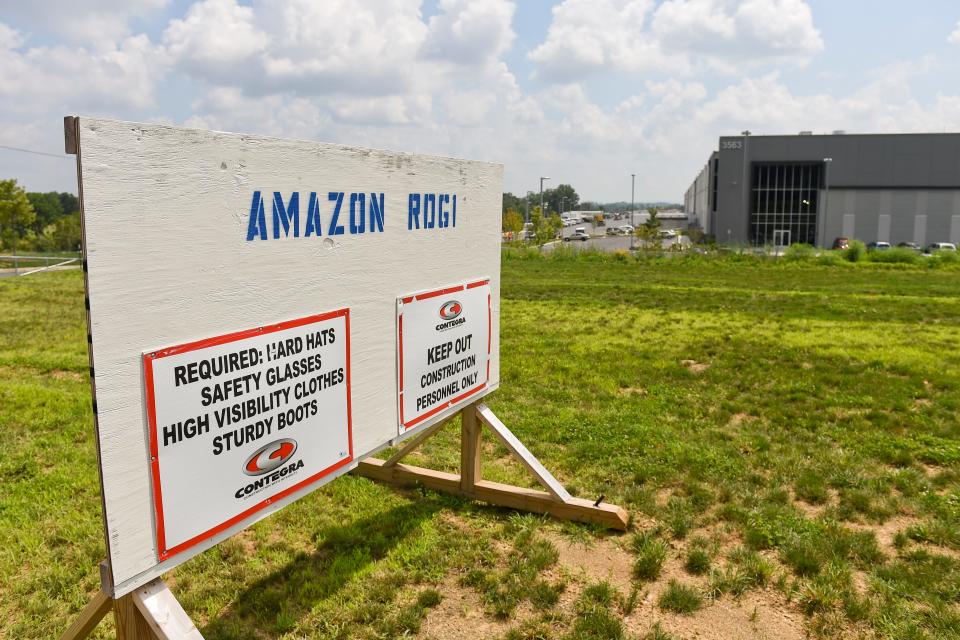 A wooden sign that reads: "Amazon ROG1" on the lawn outside of a large warehouse.