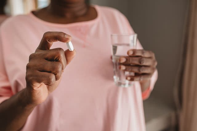 <p>Goodboy Picture Company / Getty Images</p> Closeup of a Black woman standing in her bathroom holding a vitamin and a glass of water