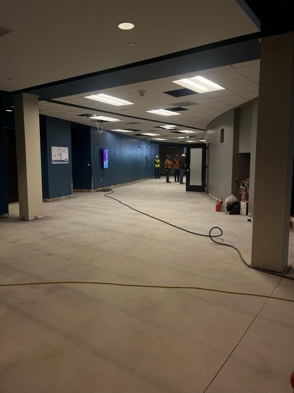 Photo inside an office building under construction. Workers stand in the distance, cables strewn about on the ground.