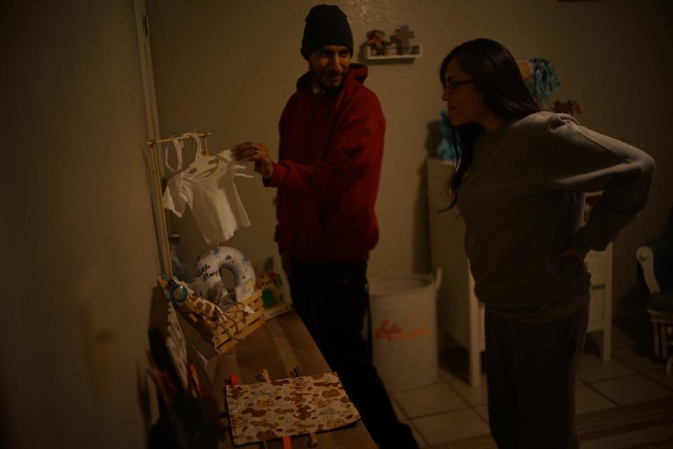 A couple stands in an apartment looking at baby clothes.