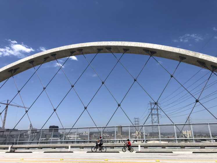 Two figures on bicycles are seen framed by one of the 6th Street Bridge's soaring arches