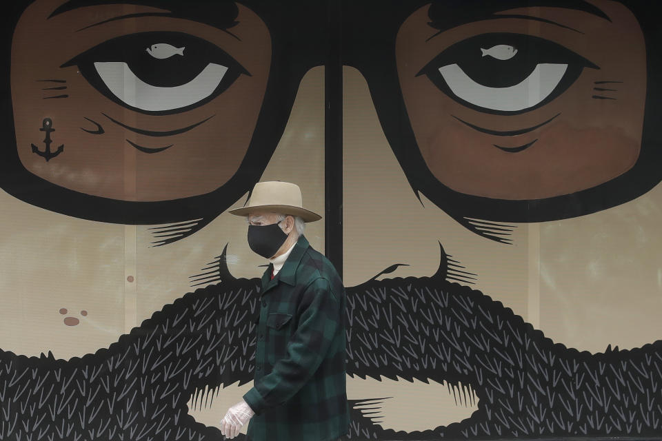 A man wears a mask while walking in front of a closed building in San Francisco, Thursday, April 16, 2020. (AP Photo/Jeff Chiu)