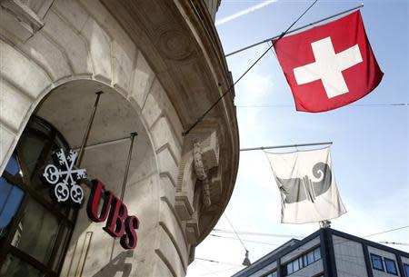 A Swiss national flag (top) and a flag of the city of Basel fly over the entrance of a branch office of Swiss bank UBS in Basel October 22, 2013. REUTERS/Arnd Wiegmann