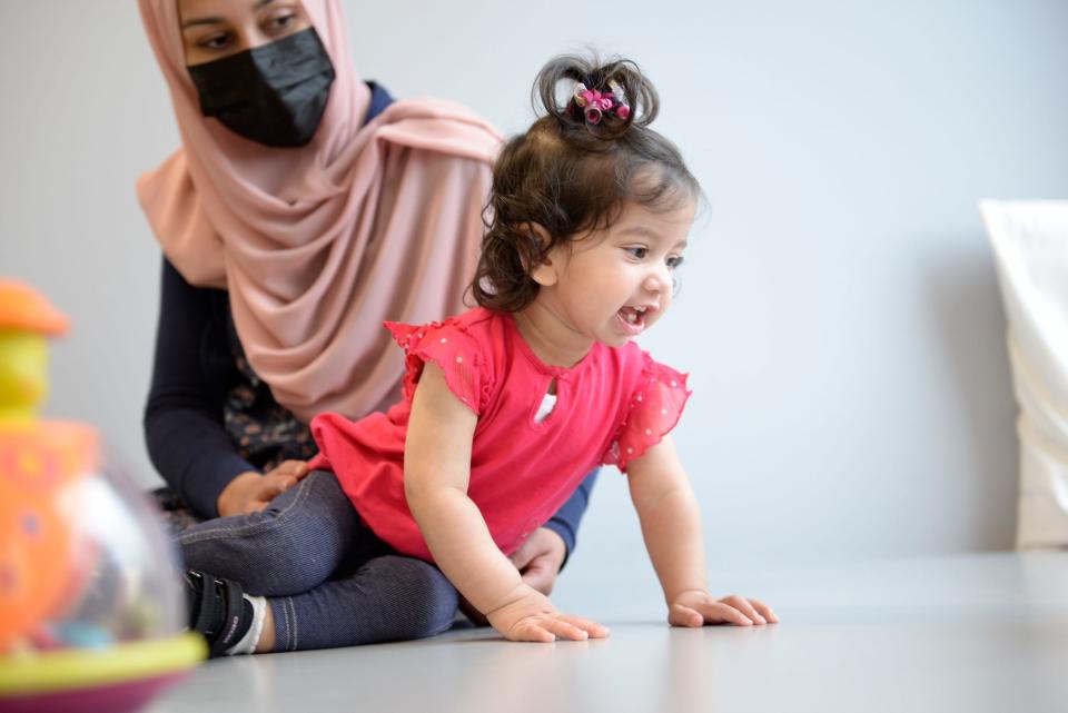 toddler smiling and crawling, mom watching behind her