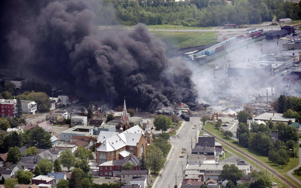 FILE - In this July 6, 2013, file photo, smoke rises from railway cars from now-defunct Montreal, Maine & Atlantic Railways company that were carrying crude oil after derailing in downtown Lac Megantic, Quebec, Canada. Attorneys general for North Dakota and Montana have petitioned the Trump administration to overrule a Washington state law that imposes safety restrictions on oil shipped by rail from the Northern Plains. Montana Attorney General Tim Fox and North Dakota's Wayne Stenehjem say in a Wednesday, July 17, 2019, petition that federal authority over railroads should pre-empt the state law. (Paul Chiasson/The Canadian Press via AP, File)