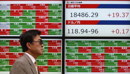 A pedestrian walks past an electronic board showing the Japan's Nikkei average (top in R top) and the exchange rates between the Japanese yen and the U.S. dollar (bottom in R top) outside a brokerage in Tokyo February 24, 2015. REUTERS/Yuya Shino