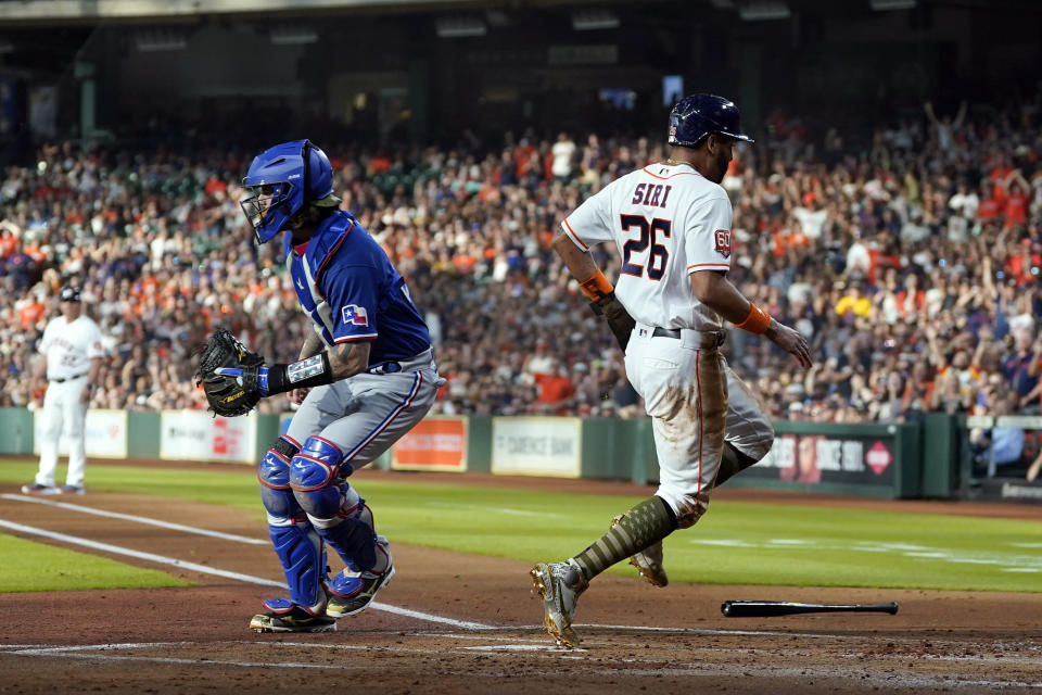 Houston Astros' Jose Siri (26) scores as Texas Rangers catcher Jonah Heim handles the throw during the first inning of a baseball game Saturday, May 21, 2022, in Houston. (AP Photo/David J. Phillip)